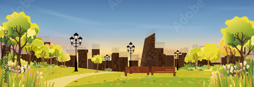 Spring landscape at city park in the morning, Natural public park with flowers blooming in the garden, Peaceful scene of green fields with blurry cityscape building, cloudy and sun on summer