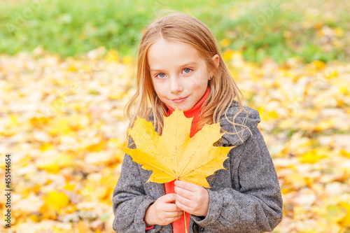 Happy young girl playing with falling yellow leaves in beautiful autumn park on nature walks outdoors. Little child holding autumn orange maple leaf.
