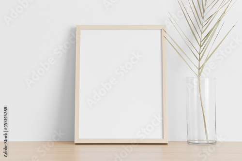 Wooden frame mockup with a palm leaf on the wooden table.