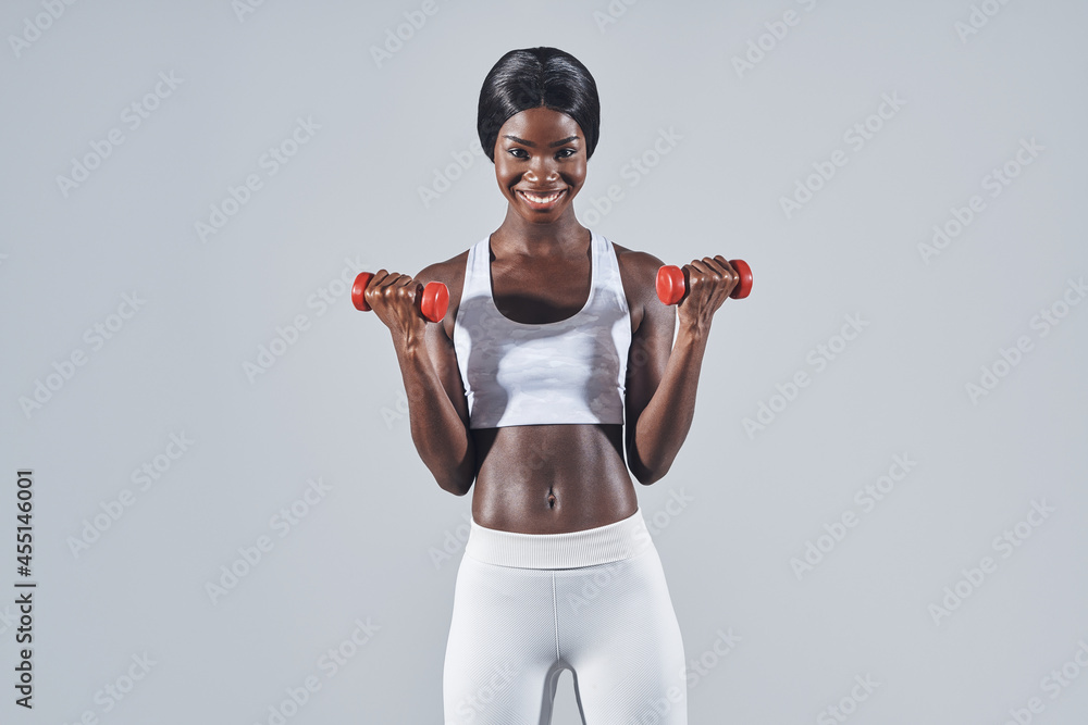Beautiful young African woman in sports clothing exercising with dumbbells Beautiful young African woman in sports clothing exercising with dumbbells