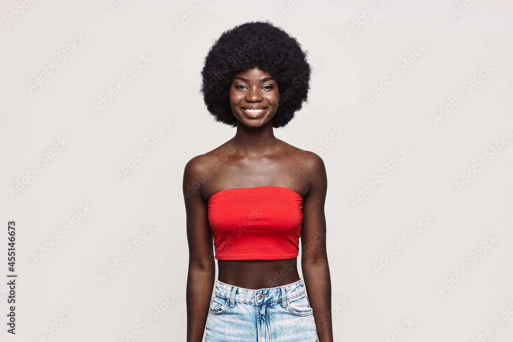 Beautiful young African woman looking at camera and smiling while standing against gray background Beautiful young African woman looking at camera and smiling while standing against gray background