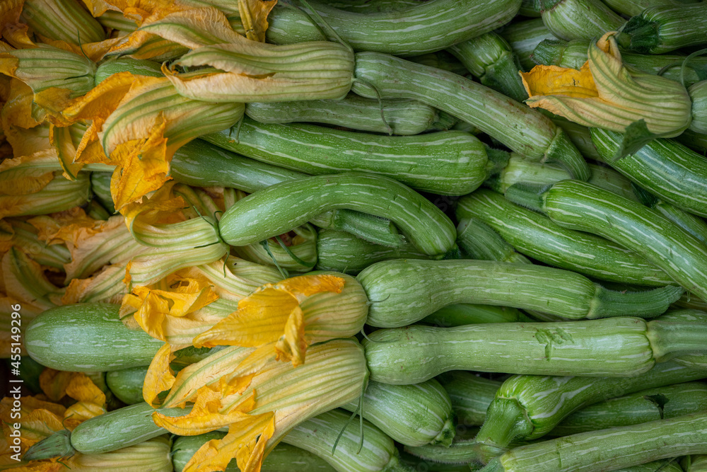 Closeup of young green zucchini vegetables with yellow flowers on the vegetable market.