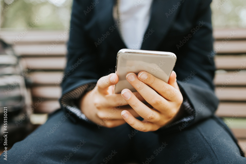 cute schoolboy with backpack in a school uniform with wireless headphones and using mobile phone is sitting on bench in the school yard, concept back to school and start of lessons cute schoolboy with backpack in a school uniform with wireless headphones and using mobile phone is sitting on bench in the school yard, concept back to school and start of lessons
