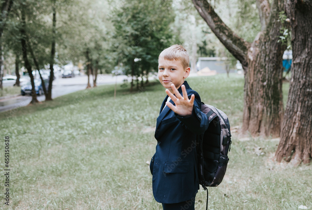 Fototapeta premium cute blond boy in a school uniform and with backpack on his shoulders goes to school at the beginning of the new school year, back to school concept and no desire to study