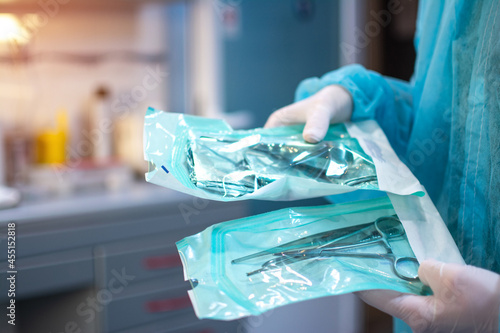 Close up of dentist hands in white sterile gloves holding dental tools for surgical use packed in a protective foil at dental office photo
