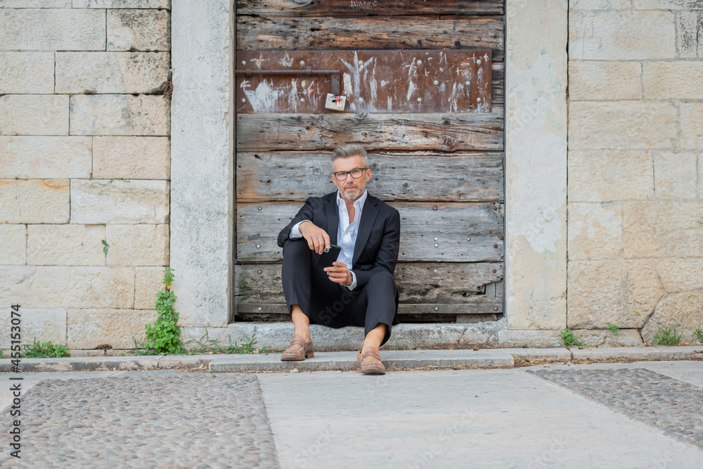 A handsome young businessman sitting on the stairs and using his smartphone..Entrepreneur working in the park and texting in a mobile phone sitting on a stair