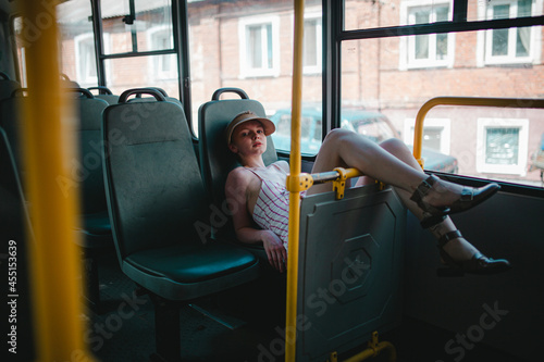 a girl with short hair, in a baseball cap, in a dress, is riding alone on a bus, a beautiful girl with short hair, wearing a hat on the bus smiles