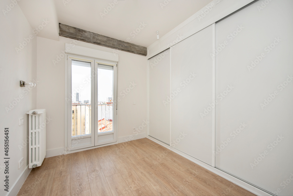 Fototapeta premium Bedroom with wall covered by a large white built-in wardrobe on one side and window leading to the terrace