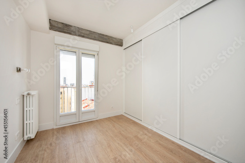 Bedroom with wall covered by a large white built-in wardrobe on one side and window leading to the terrace