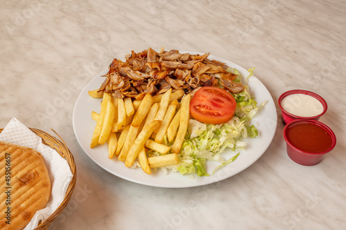 Chicken meat kebab menu with french fries, iceberg salad, tomato sauce, yogurt sauce and tomato sauce and pita bread on white marble table