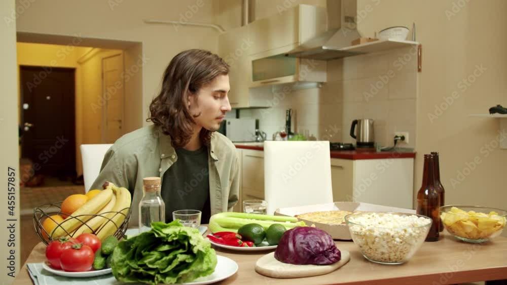 One of friends is sitting down at the table while his pal is entering the kitchen One of friends is sitting down at the table while his pal is entering the kitchen