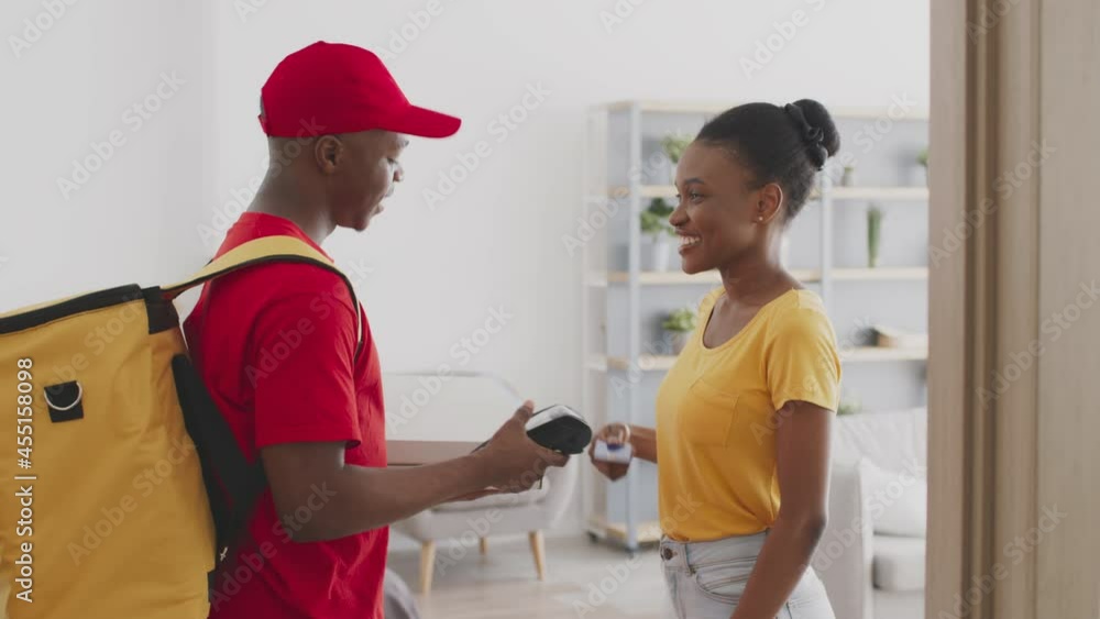 Young positive african american lady paying for pizza with credit card to courier, smiling to delivery man at home Young positive african american lady paying for pizza with credit card to courier, smiling to delivery man at home