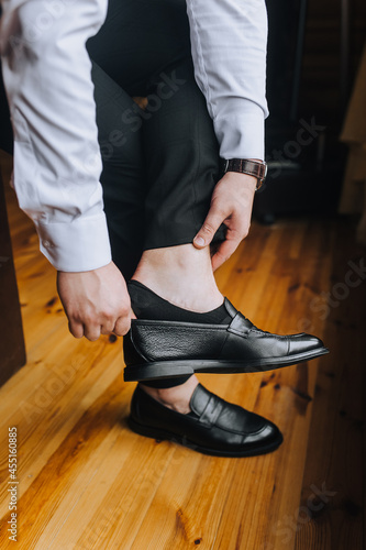 A man businessman in a white shirt puts black shiny shoes on his feet, going to work in the morning. Business photography.
