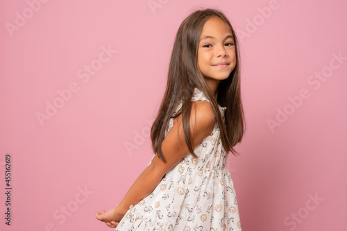 Beautiful smiling little girl in white dress isolated over pink background.