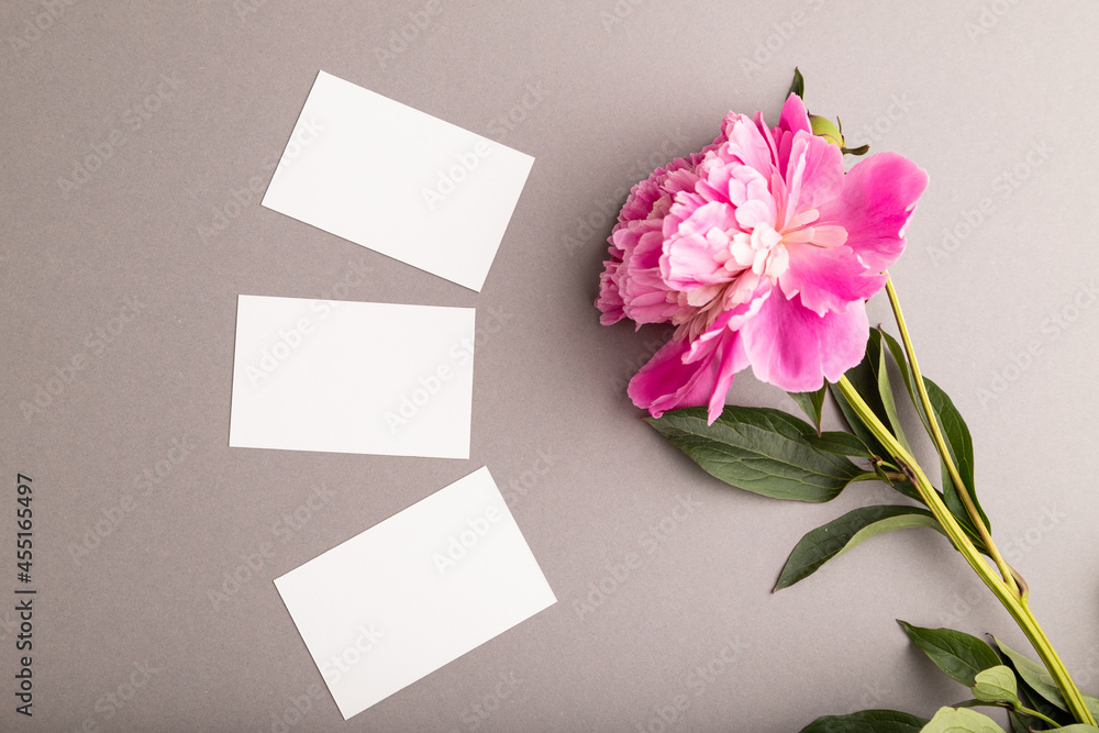 White business card with pink peony flowers on gray pastel background. top view, copy space. White business card with pink peony flowers on gray pastel background. top view, copy space.