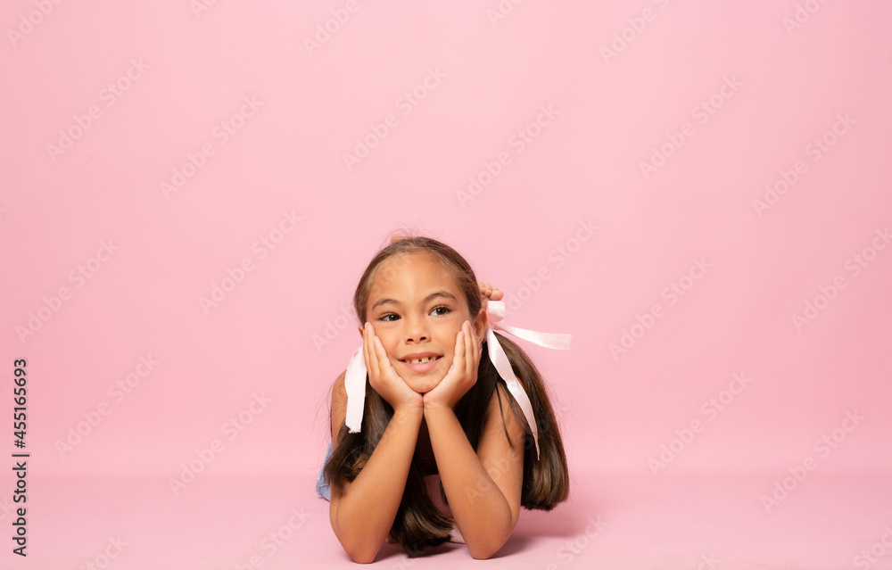 Beautiful smiling little girl lying on the floor isolated over pink background. Beautiful smiling little girl lying on the floor isolated over pink background.
