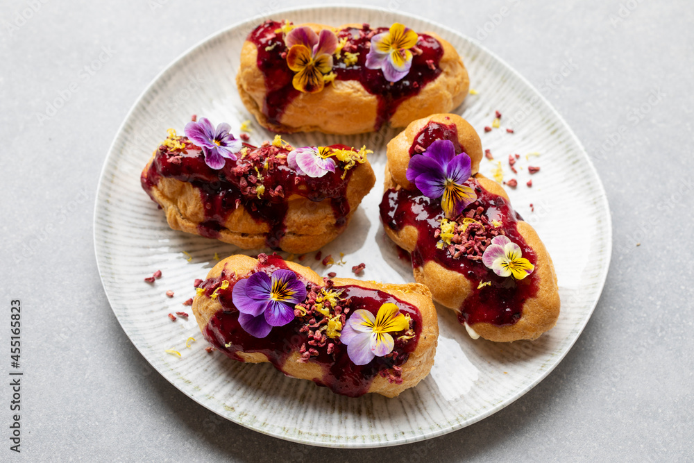 Small eclairs with bluberry icing and violet flowers