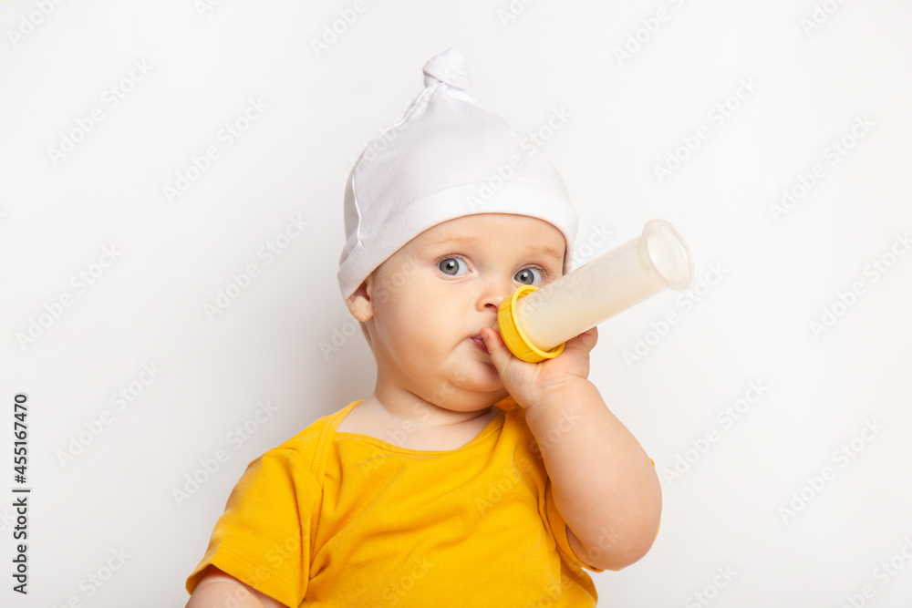 portrait of a cute happy caucasian baby boy dressed in a yellow t-shirt and a hat on white background. child drinks milk from a bottle with copyspace. nutrition and healthcare concept portrait of a cute happy caucasian baby boy dressed in a yellow t-shirt and a hat on white background. child drinks milk from a bottle with copyspace. nutrition and healthcare concept