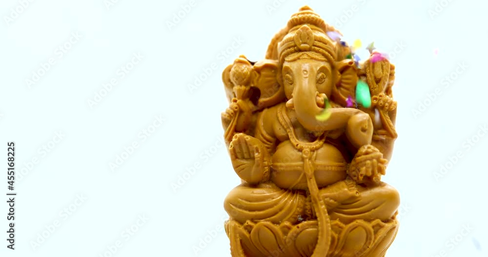Ganesh Chaturthi Concept: Statue of the Hindu god Ganapati with a white background. Confetti Embellishments fell Ganesh Chaturthi Concept: Statue of the Hindu god Ganapati with a white background. Confetti Embellishments fell