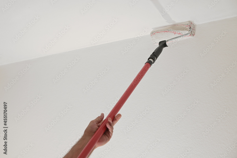 Hand of a man holding a paint roller on a long telescopic pole to paint the ceiling while renovating an apartment, housing concept, copy space, selected focus - obrazy, fototapety, plakaty 