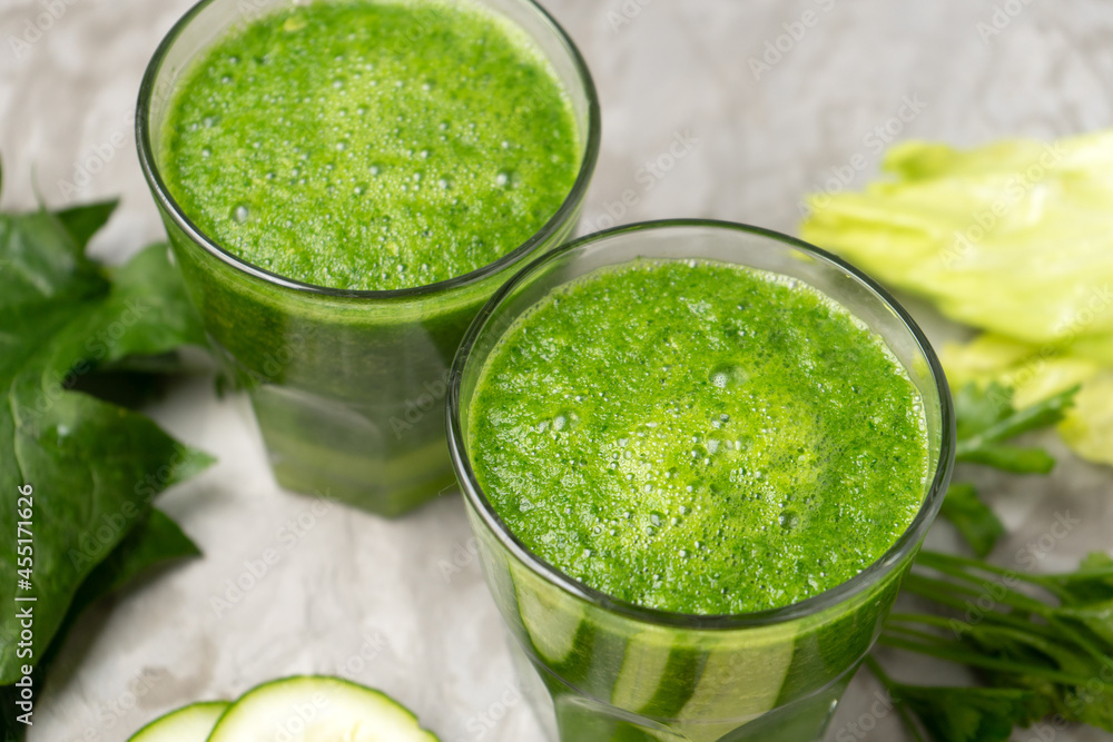 Green juice and ingredients in glass on grey background Green juice and ingredients in glass on grey background