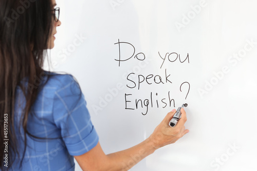 Woman teacher writes with marker do you speak english on white board photo