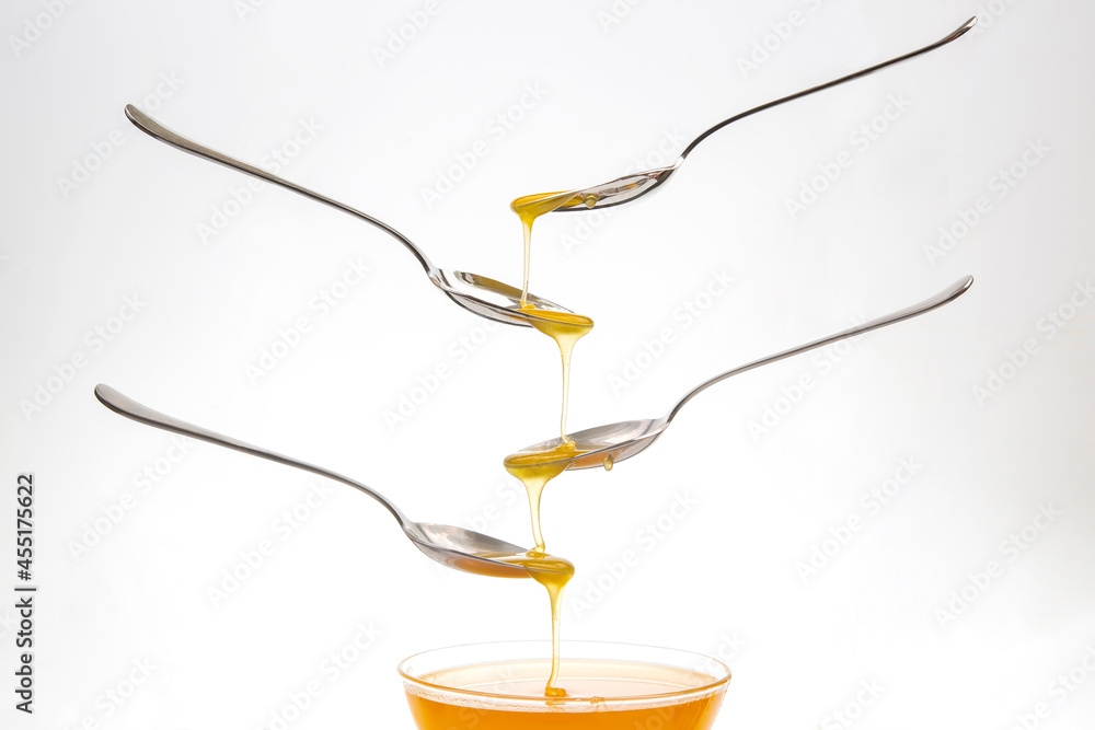 Fresh flower honey drips from a spoon into a spoon on a white background. Organic vitamin food. Fresh flower honey drips from a spoon into a spoon on a white background. Organic vitamin food.