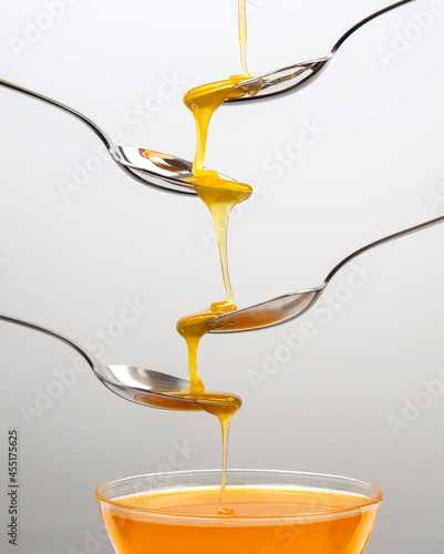 Fresh flower honey drips from a spoon into a spoon on a light background. Organic vitamin food.