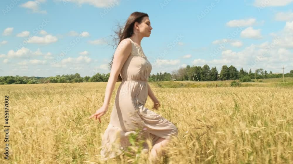 attractive young woman in white dress runs across yellow field against blue sky with clouds. beauty lady is in hurry to meet her beloved in rye. Fashion video in slow motion. attractive young woman in white dress runs across yellow field against blue sky with clouds. beauty lady is in hurry to meet her beloved in rye. Fashion video in slow motion.