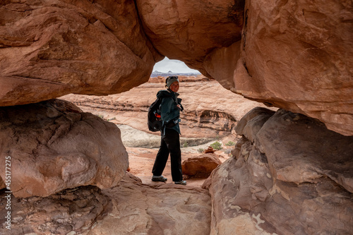 Hiker Dressed For Rain Looks Back Through Hole In The Canyon Wall