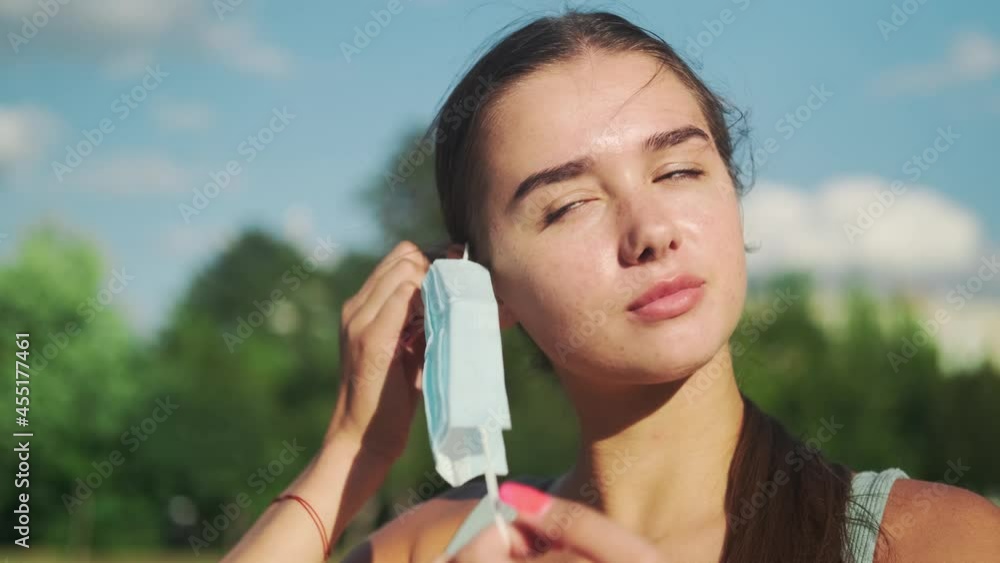 A beautiful sportive girl in nature takes off the medical mask and smiles. Close-up. Slow motion. 4k footage A beautiful sportive girl in nature takes off the medical mask and smiles. Close-up. Slow motion. 4k footage
