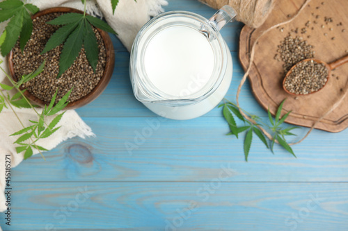 Hemp milk, seeds and leaves on light blue wooden background, flat lay. Space for text