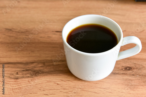 White cup of strong black coffee on wooden surface close up