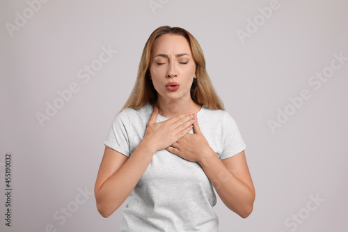 Young woman suffering from pain during breathing on light grey background photo