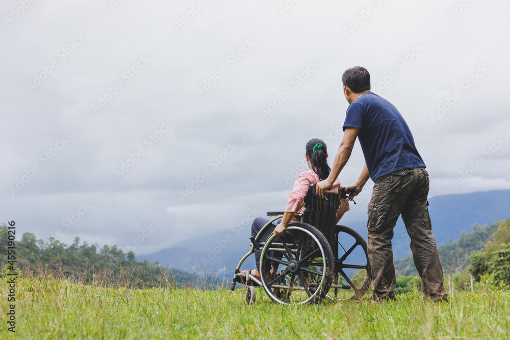 Male pushing wheelchair with disabled woman looking sky on mountain park Male pushing wheelchair with disabled woman looking sky on mountain park