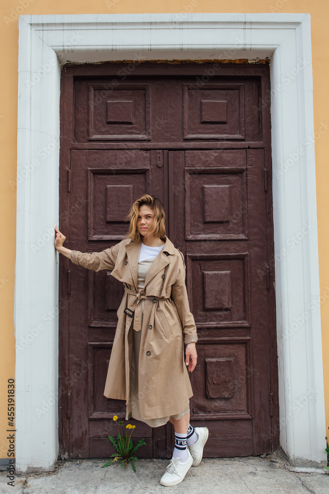 Young millennial woman with wild hair dressed in an autumn coat posing near the door of an old building. Young millennial woman with wild hair dressed in an autumn coat posing near the door of an old building.