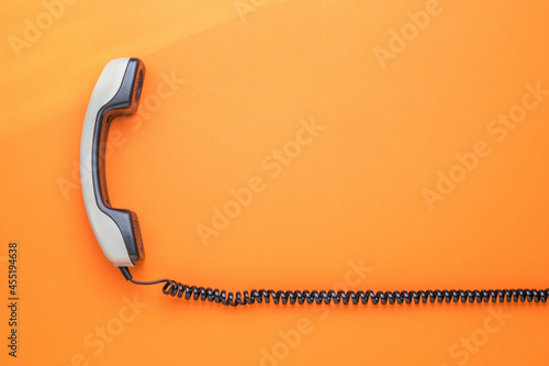 A gray handset with a wire on an orange background. Flat lay. photo