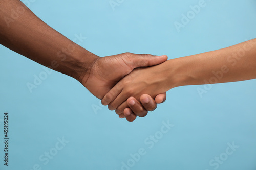 Woman and African American man shaking hands on light blue background, closeup