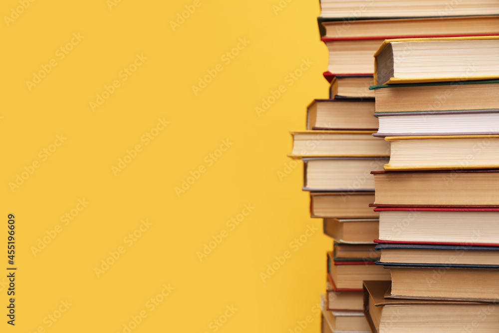 Many hardcover books on orange background, space for text. Library material - obrazy, fototapety, plakaty 