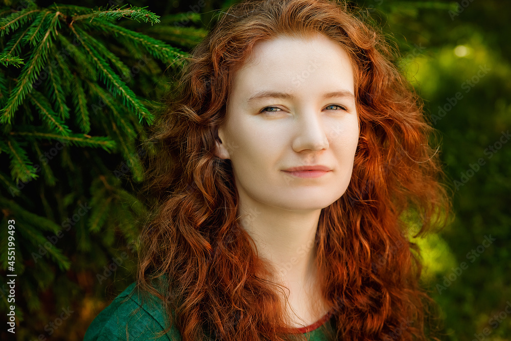 A large portrait of a beautiful red-haired woman against the background of greenery in the park. A large portrait of a beautiful red-haired woman against the background of greenery in the park.
