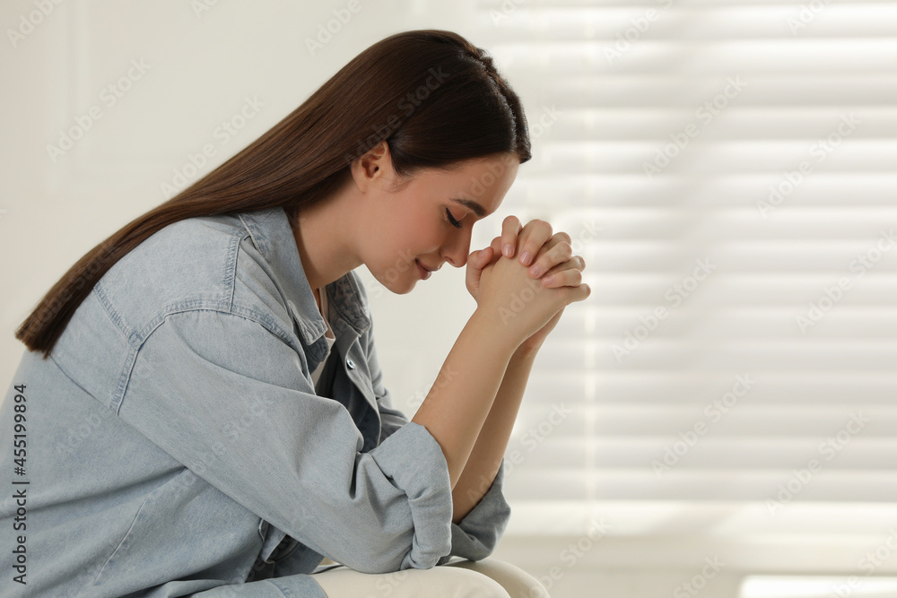 Religious young woman with clasped hands praying indoors Religious young woman with clasped hands praying indoors