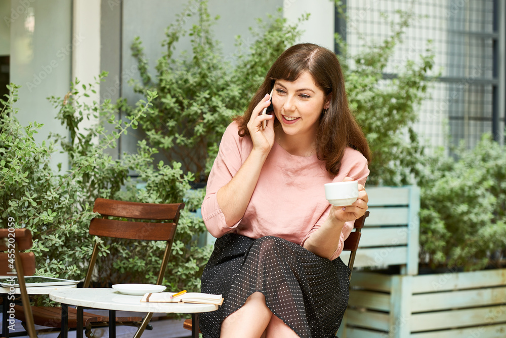 Happy young woman drinking morning coffee in coffeeshop and talking on phone with friend Happy young woman drinking morning coffee in coffeeshop and talking on phone with friend