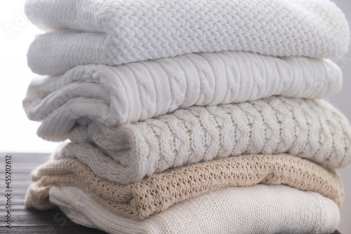 Stack of white cozy knitted sweaters on wooden table