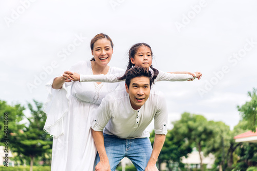 Portrait of enjoy happy love asian family father and mother holding little asian girl on back smiling playing and having fun moments good time in summer park at home