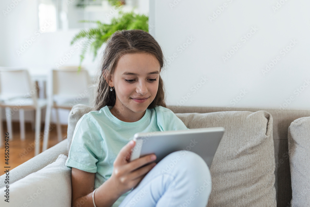 cute little happy girl smile sitting down on sofa using looking digital tablet pad in the living room at home. family activity concept.