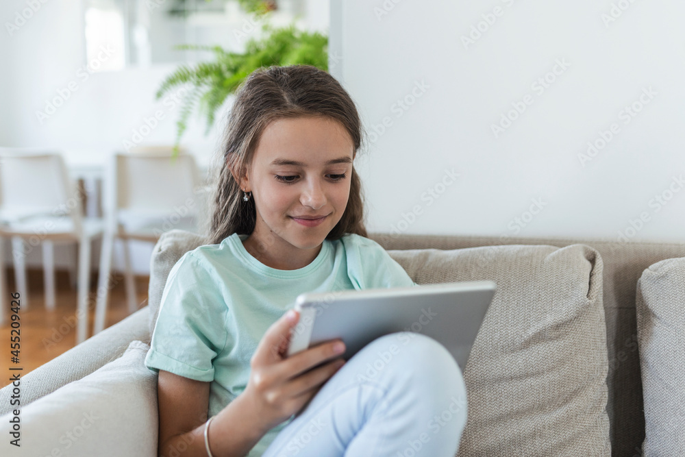 cute little happy girl smile sitting down on sofa using looking digital tablet pad in the living room at home. family activity concept. cute little happy girl smile sitting down on sofa using looking digital tablet pad in the living room at home. family activity concept.
