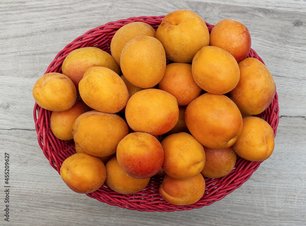 Fresh apricots in a red basket on a wooden table. View from above