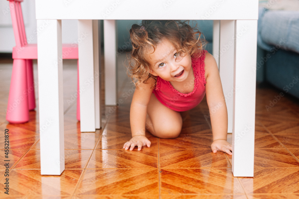 childhood and people concept - happy two years old baby girl playing under a table at home childhood and people concept - happy two years old baby girl playing under a table at home