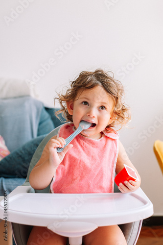 Cute funny baby girl 2 years old sitting with a spoon in his mouth.