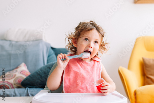 Cute funny baby girl 2 years old sitting with a spoon in his mouth.
